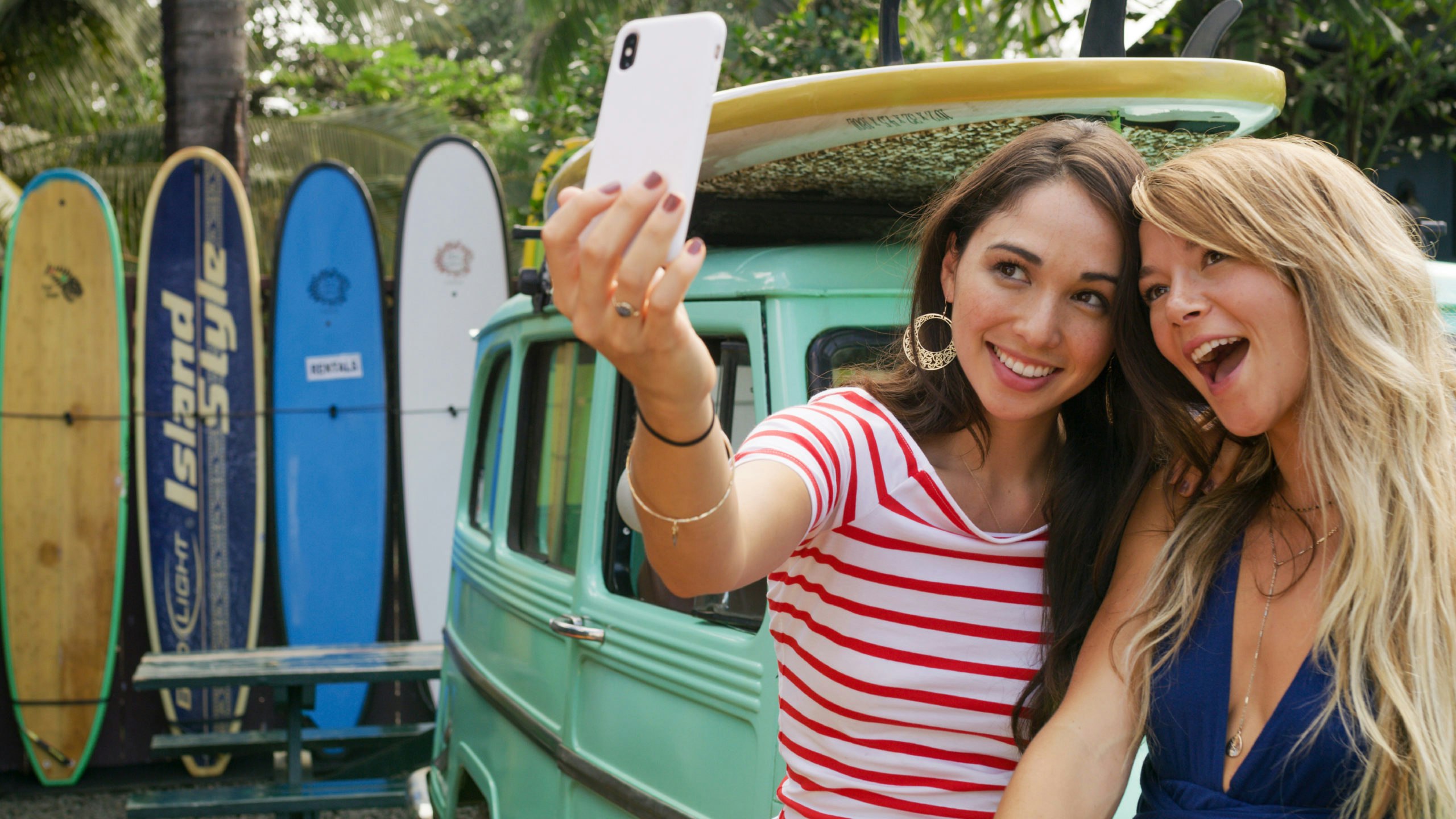 Two women standing in front of van and surfboards take a selfie