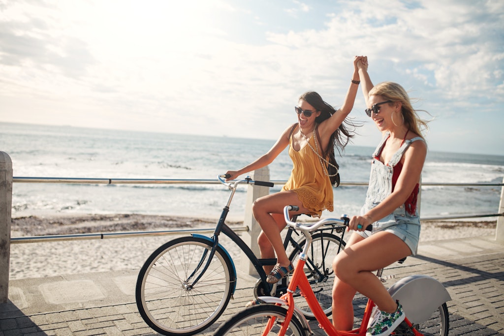 Two girls riding bikes by the beach