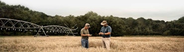 Two farmers standing in a field in front of an irrigation system